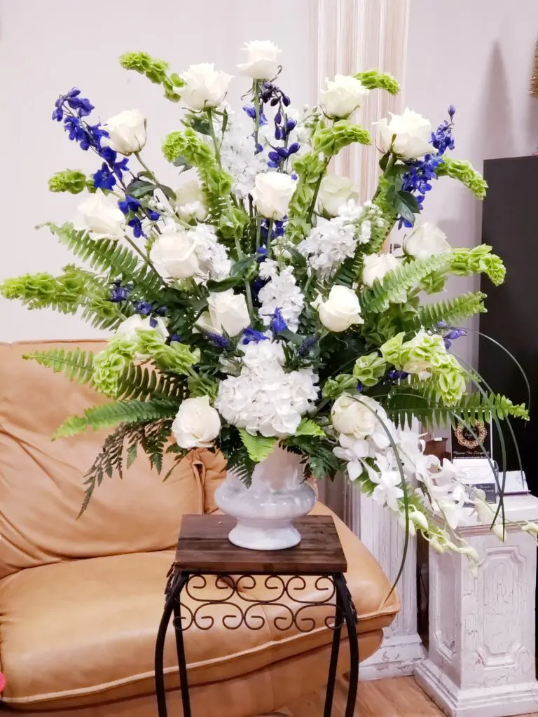 A large vase filled with white and blue flowers is sitting on a table in a living room.