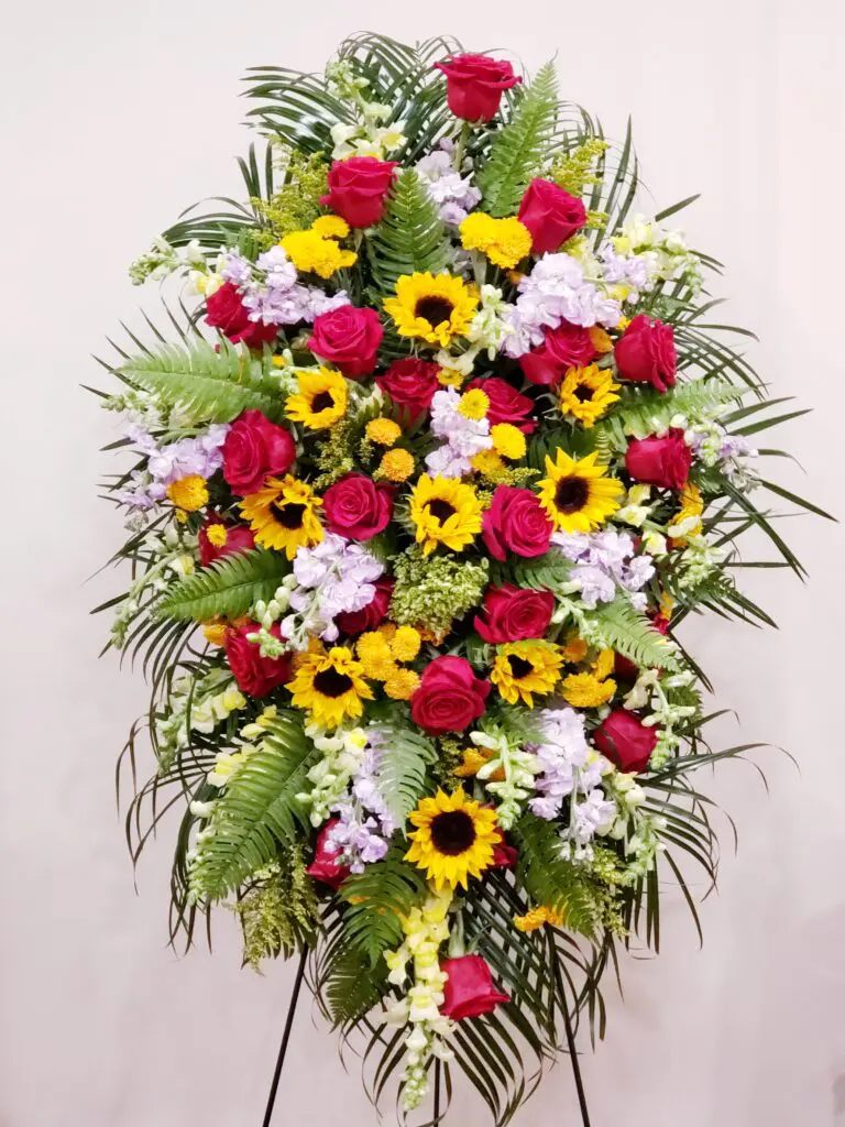 A wreath of red roses , sunflowers , and other flowers on a stand.