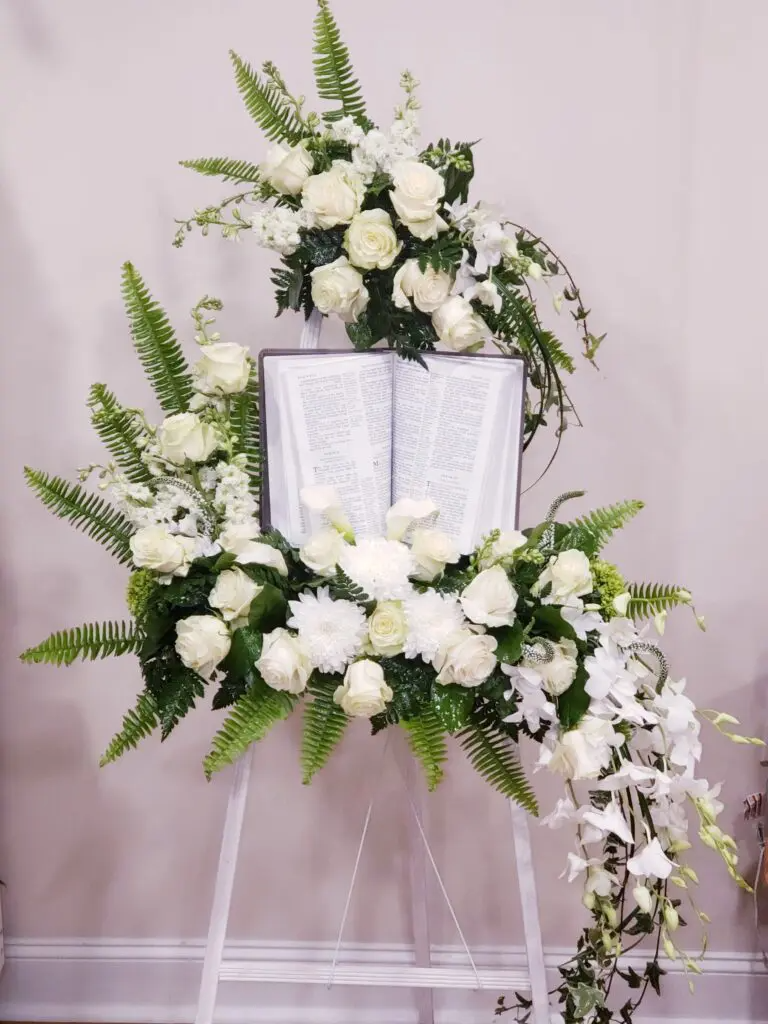 A bible is surrounded by white flowers on a white easel.