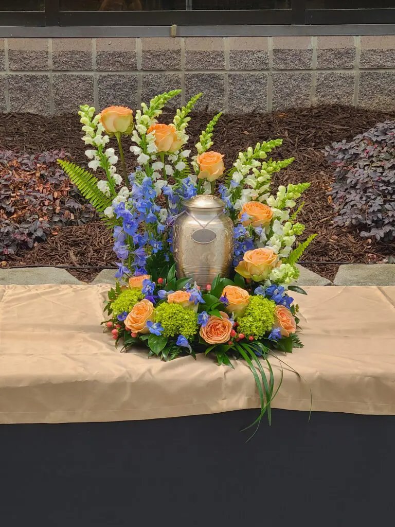 A urn is surrounded by flowers on a table.