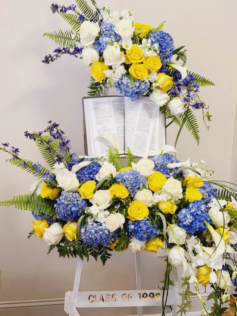 A display of blue and yellow flowers with a bible on top of it.