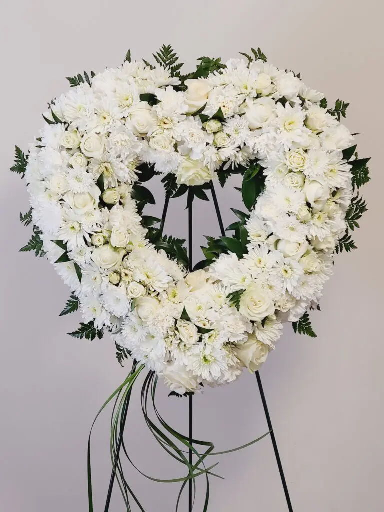 A heart shaped wreath made of white flowers is on a stand.