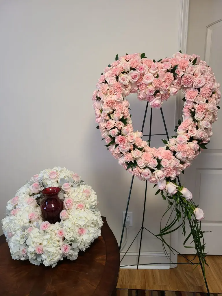 A wreath in the shape of a heart is sitting on a table next to a vase of flowers.