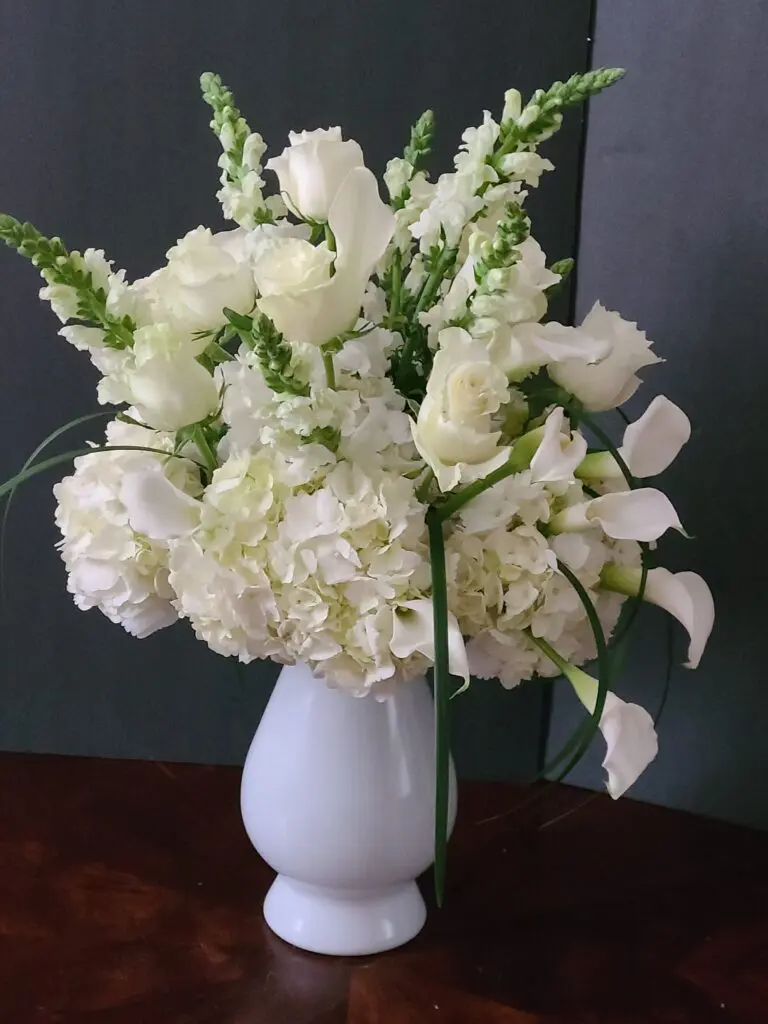 A white vase filled with white flowers on a table