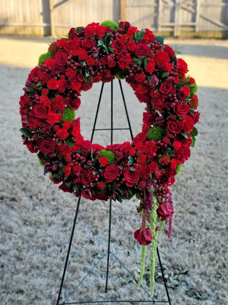 A wreath made of red roses and carnations is sitting on a metal stand.