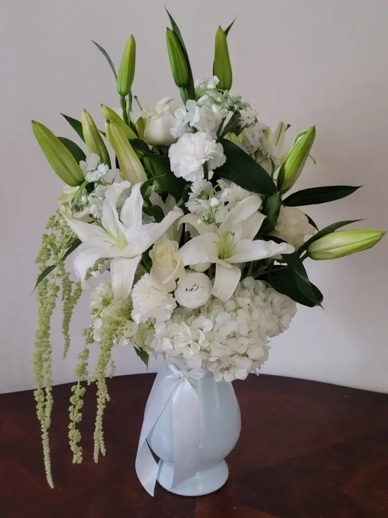 A white vase filled with white flowers is sitting on a table.