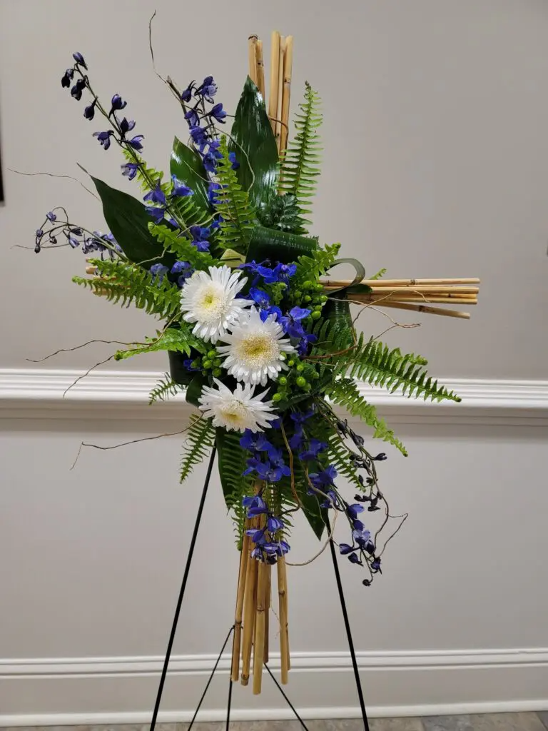 A cross made of sticks and flowers is sitting on a stand.