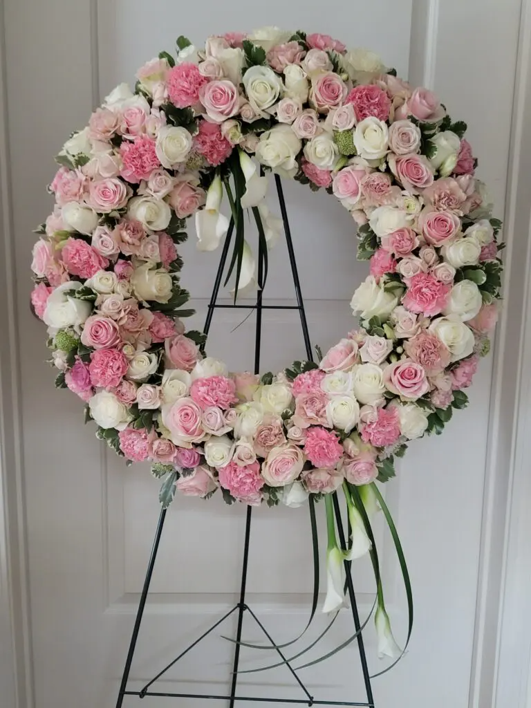 A wreath of pink and white flowers is sitting on a metal stand.