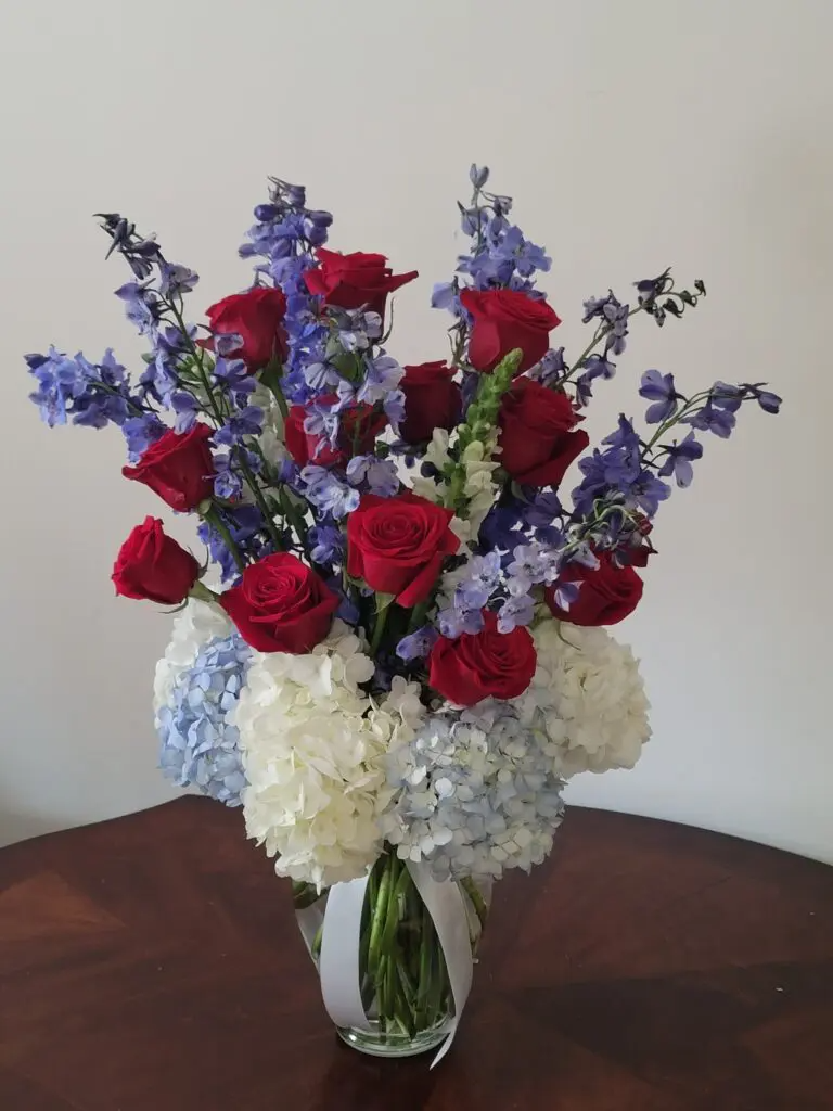 A vase filled with red , white and blue flowers on a table.