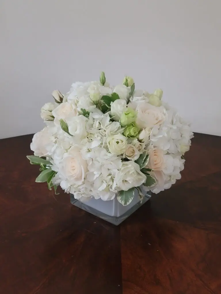 A vase filled with white flowers is sitting on a wooden table.