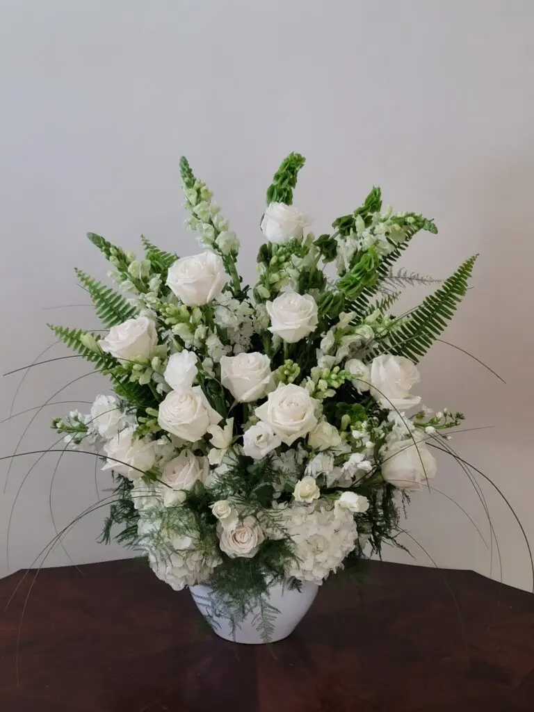 A vase filled with white flowers and greenery is sitting on a table.