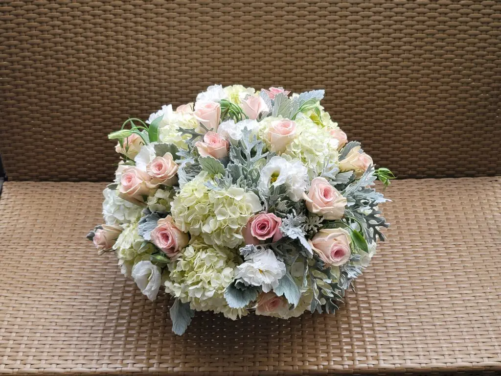 A bouquet of flowers is sitting on a wicker bench.