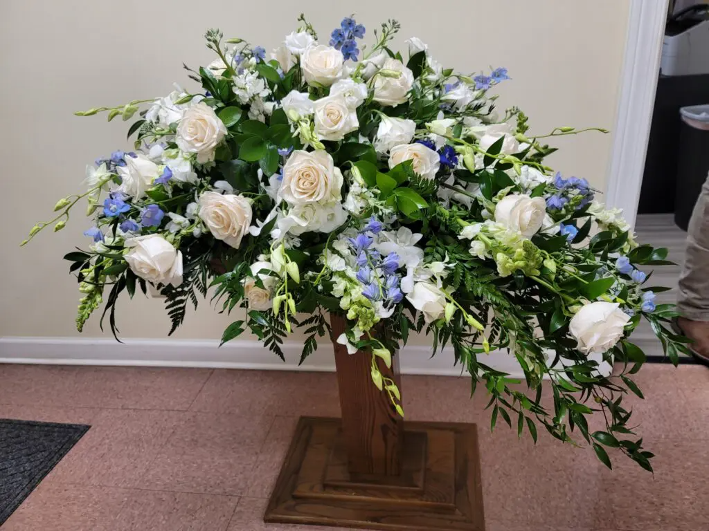 A large bouquet of white and blue flowers on a wooden stand.