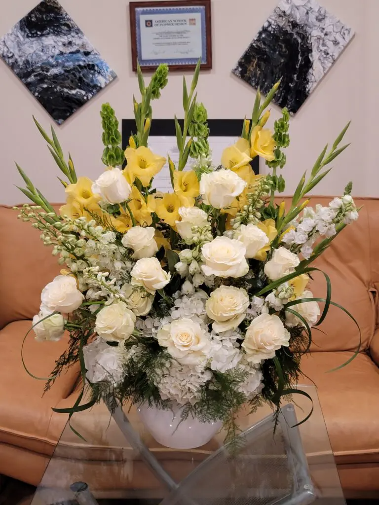 A vase filled with yellow and white flowers is sitting on a glass table.