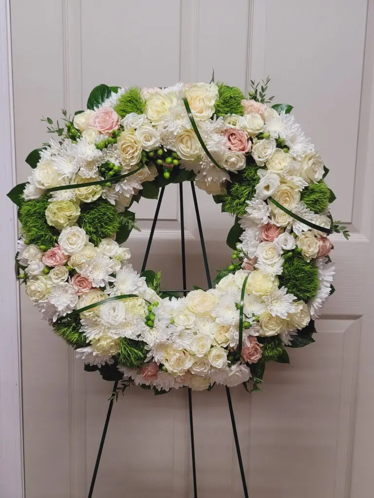 A wreath of white flowers is sitting on a stand in front of a door.