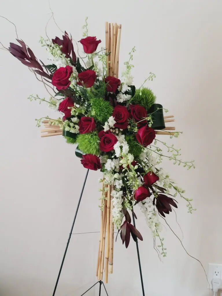 A cross with red roses and greenery on a stand