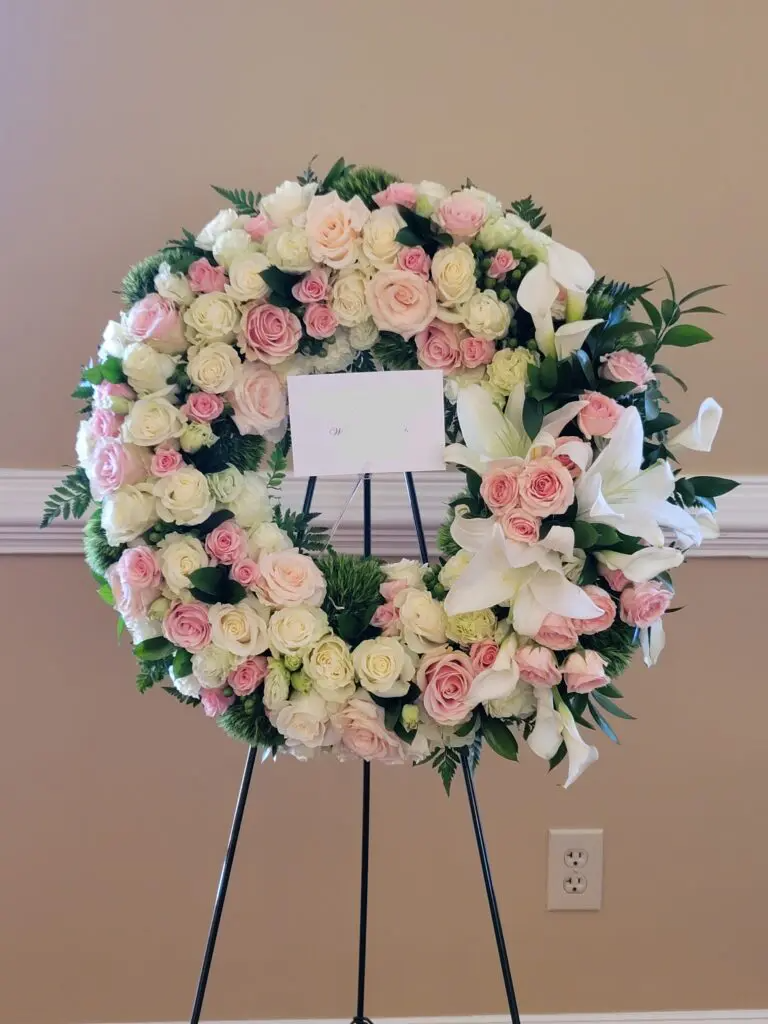 A wreath of pink and white flowers is sitting on a stand.