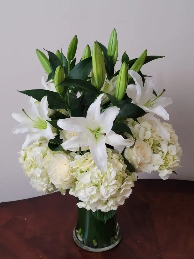 A vase filled with white flowers is sitting on a wooden table.