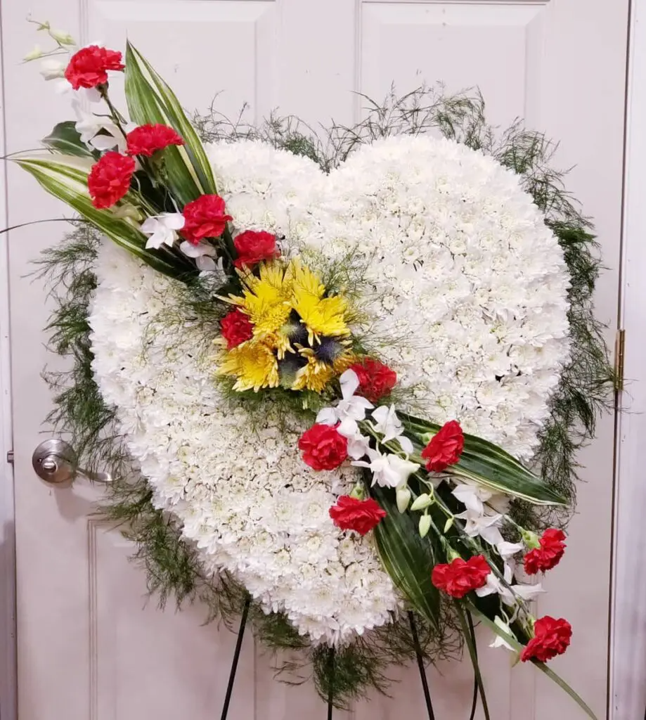 A heart shaped wreath made of white flowers and red carnations