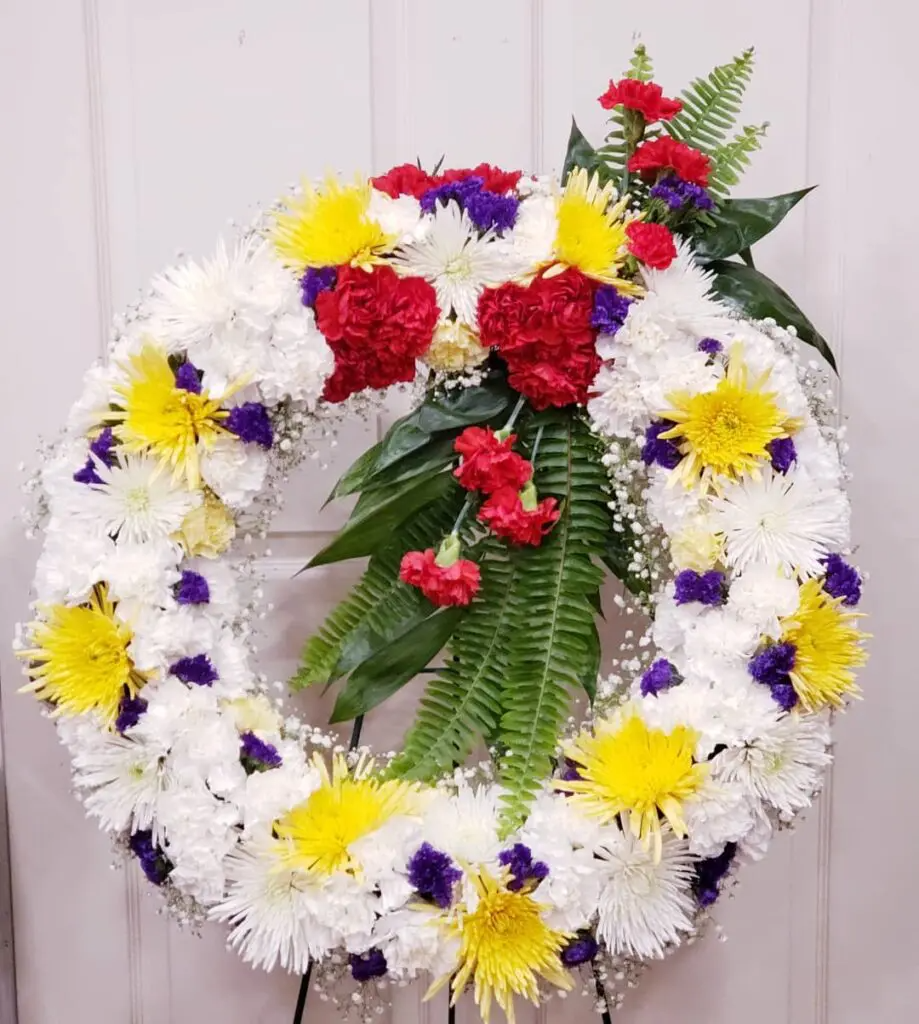 A wreath with red , yellow and purple flowers is sitting on a stand.