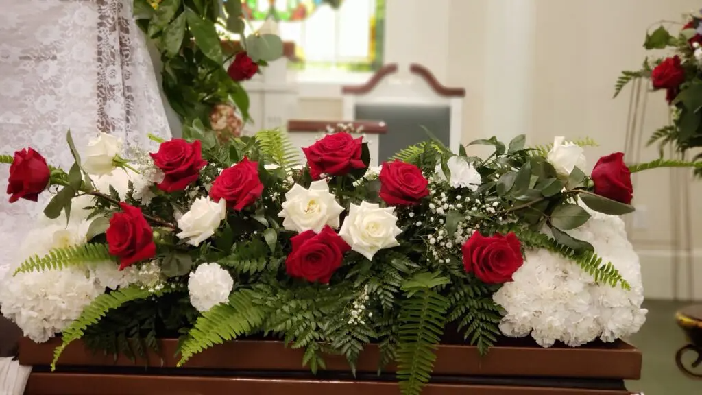 A coffin decorated with red and white roses and carnations in a church.