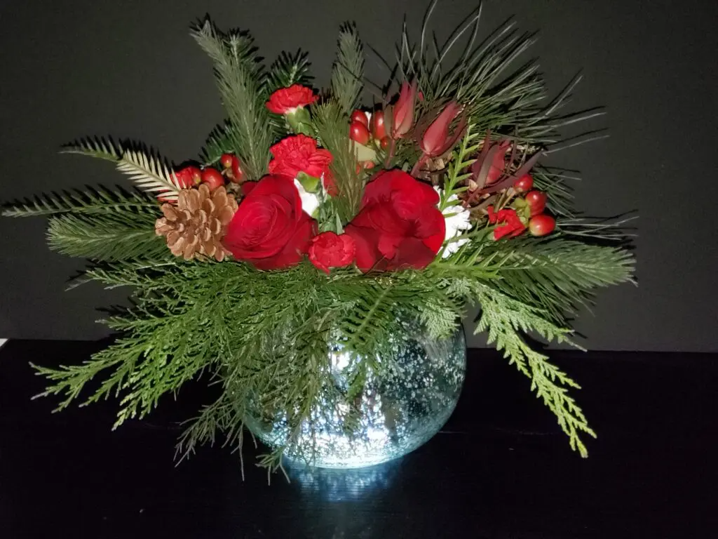A vase filled with red flowers and greenery is sitting on a table.