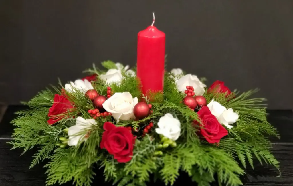 There is a red candle in the middle of a flower arrangement.