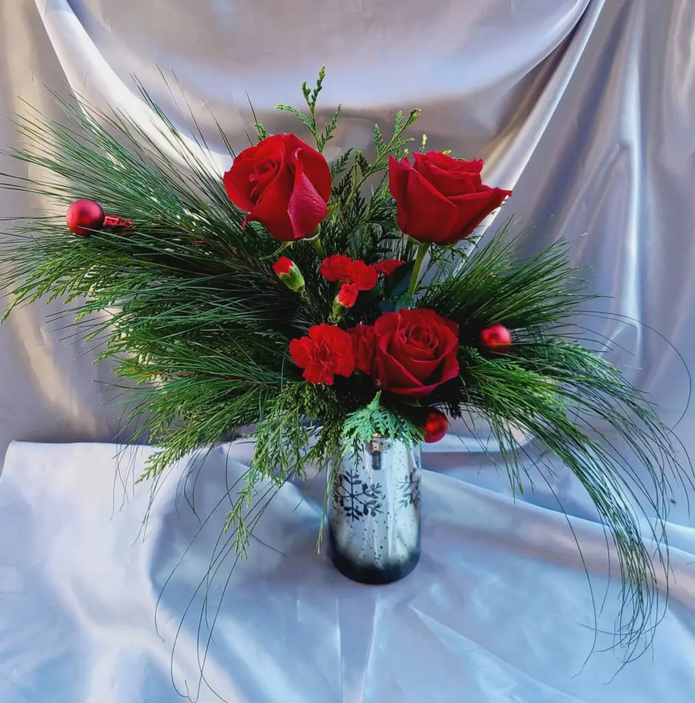 A silver vase filled with red roses and greenery