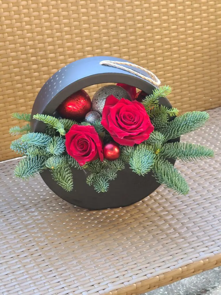 A black basket filled with red roses and christmas decorations.