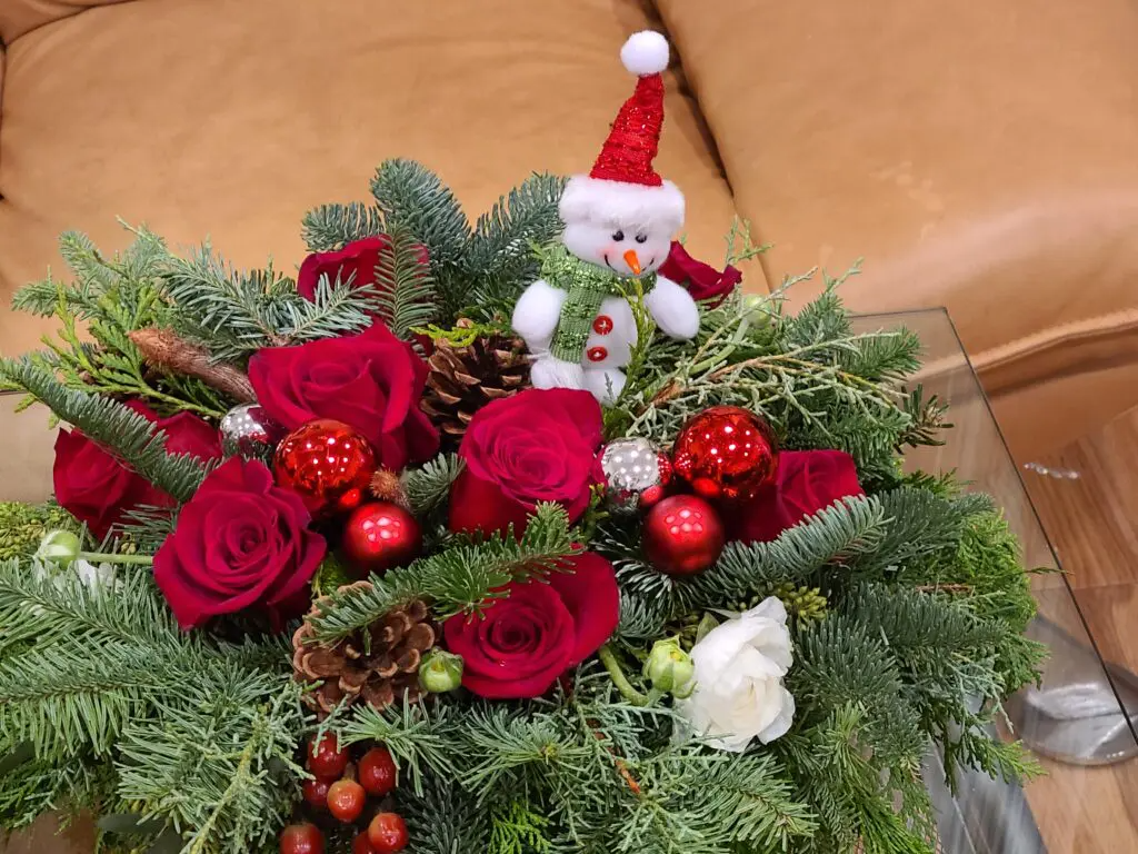 A christmas arrangement with roses , pine cones , and a snowman on top of it.