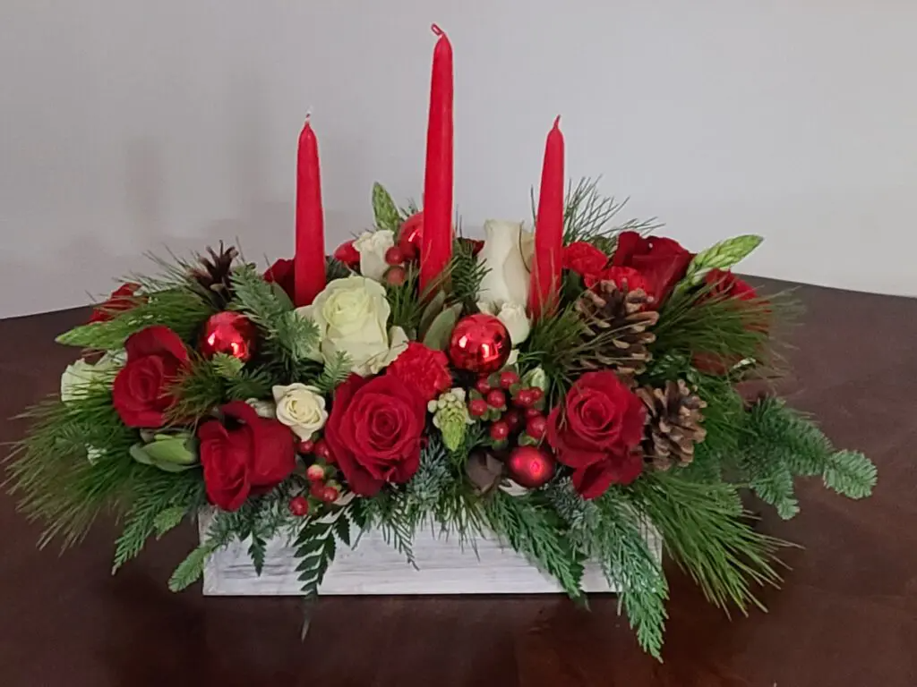 A christmas centerpiece with red candles and red roses on a table.