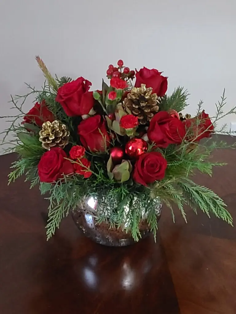 A vase filled with red roses , pine cones , and christmas ornaments on a table.