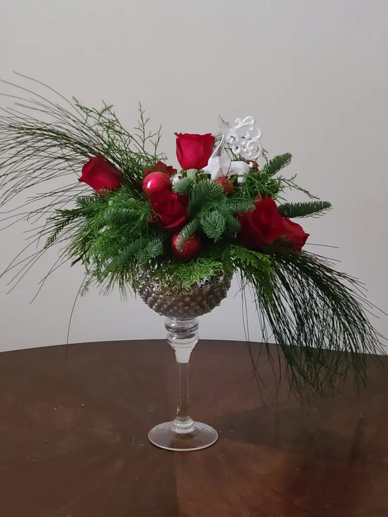 A vase filled with red roses and greenery is sitting on a table.