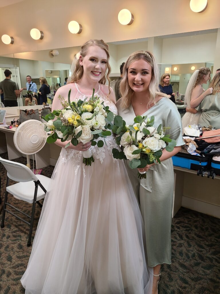 A bride and her bridesmaid are posing for a picture in a dressing room.