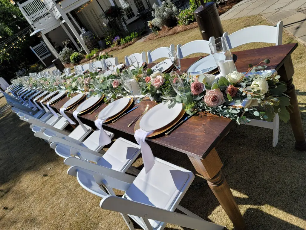 A long wooden table with white chairs and plates on it.