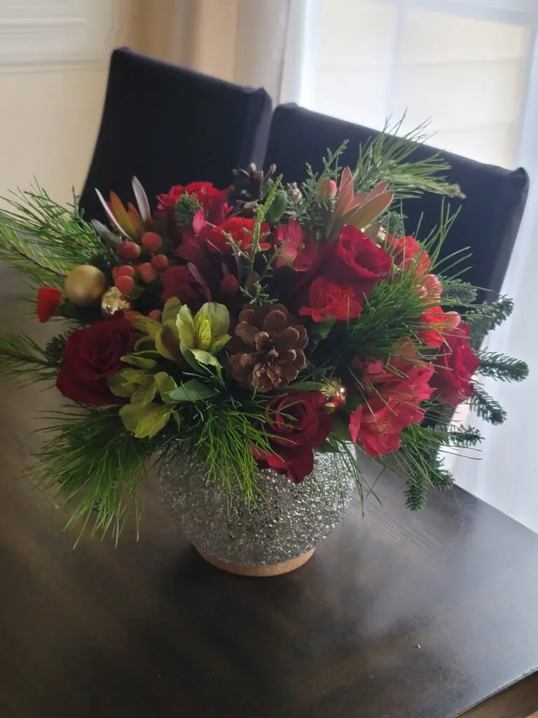A vase filled with flowers and pine cones is sitting on a table.