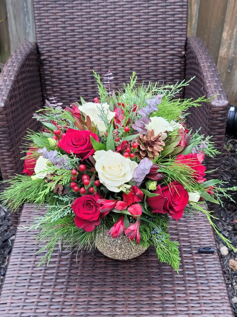 A vase filled with red and white flowers is sitting on a wicker chair.