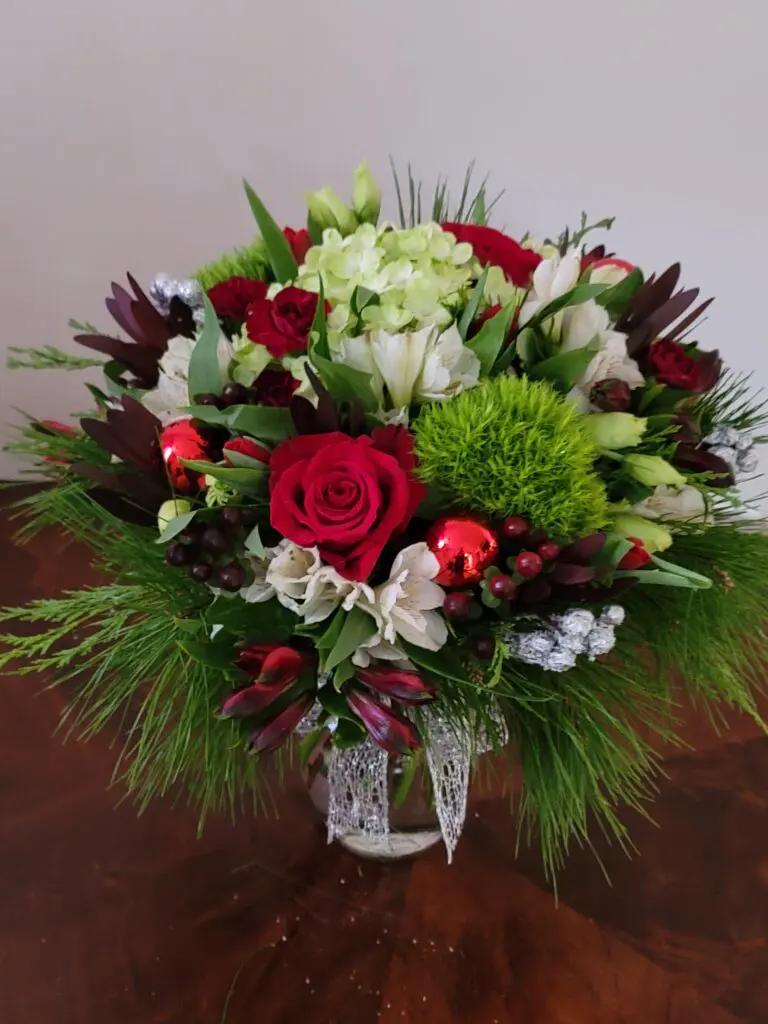 A vase filled with flowers and greenery is sitting on a wooden table.