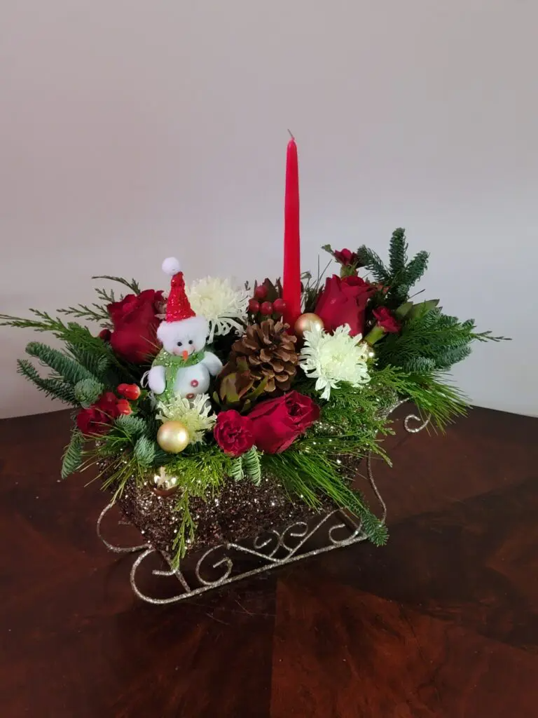 A sleigh filled with flowers and a candle on a table.