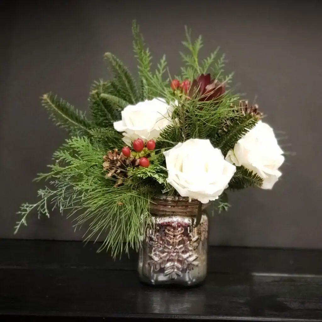 A vase filled with white roses , pine cones , and red berries.