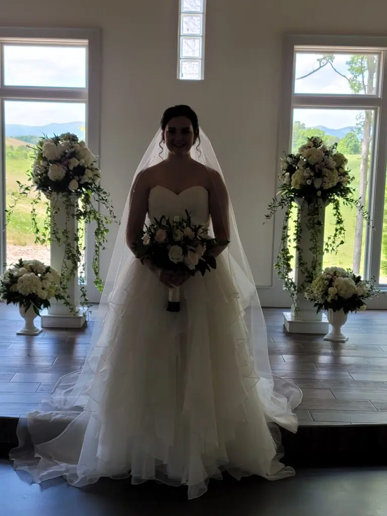 A bride in a wedding dress is standing in front of a window holding a bouquet of flowers.