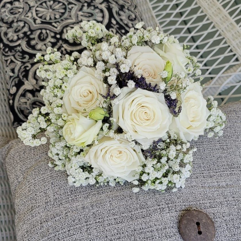 A bouquet of white roses and baby 's breath is sitting on a couch.