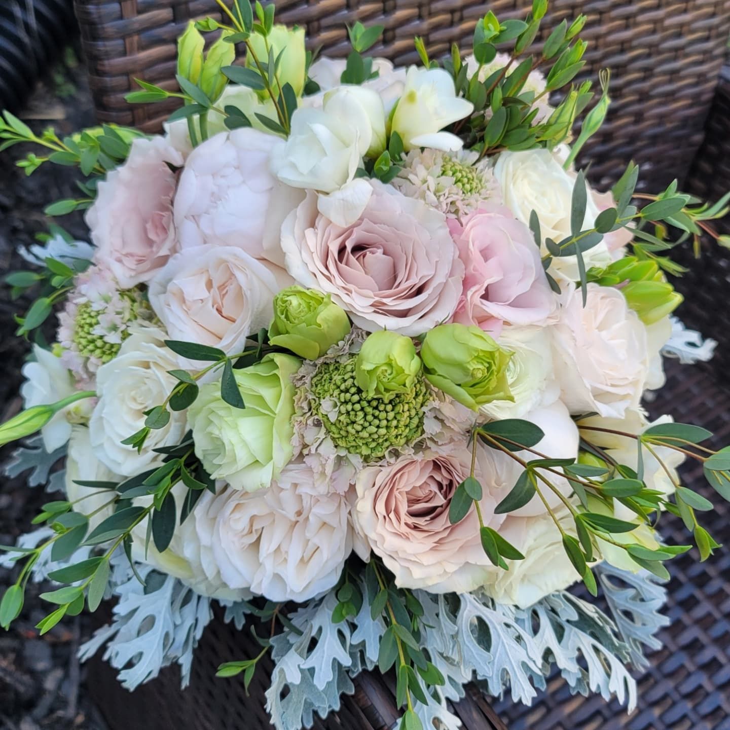 A bouquet of pink and white flowers is sitting on a wicker chair.