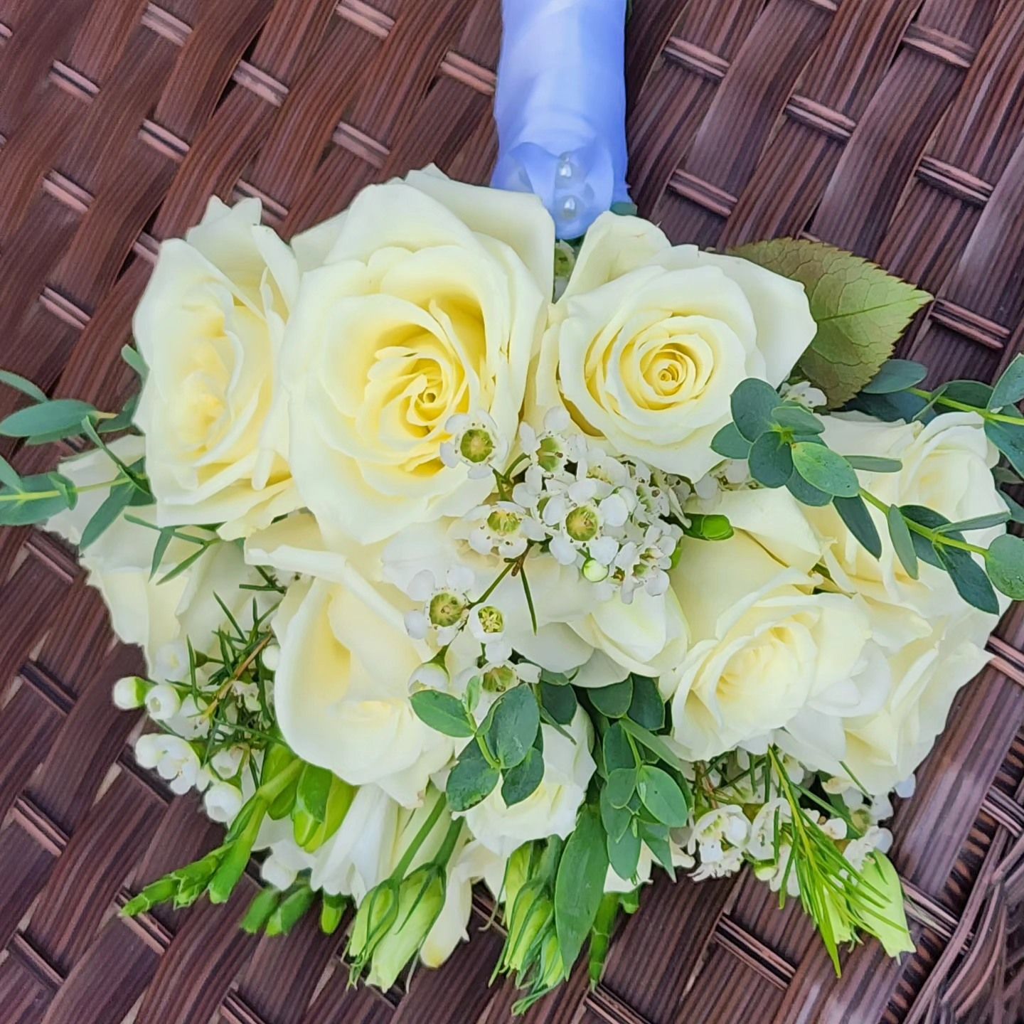 A bouquet of white roses and greenery with a blue ribbon