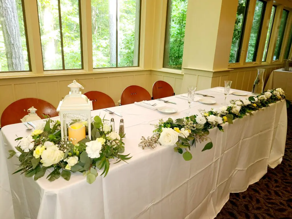 A long table with a white table cloth and flowers on it.
