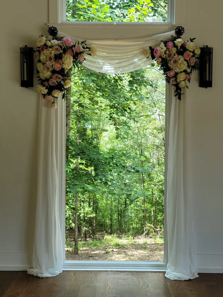 A window with flowers hanging from it and a view of a forest.