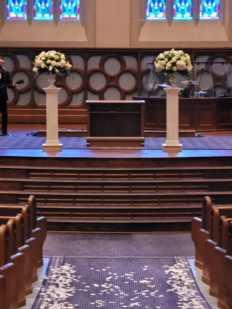 A man is standing on a stage in a church with flowers on it