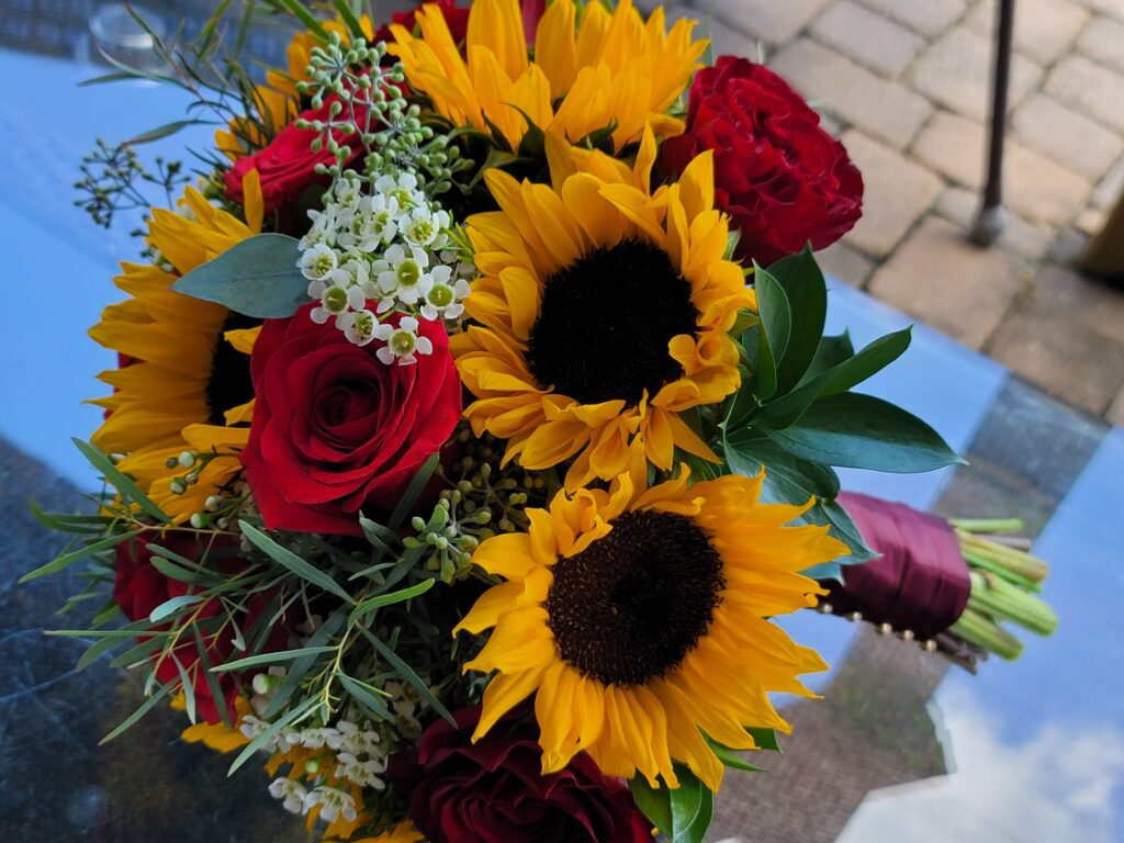 A bouquet of sunflowers and red roses is sitting on a table.