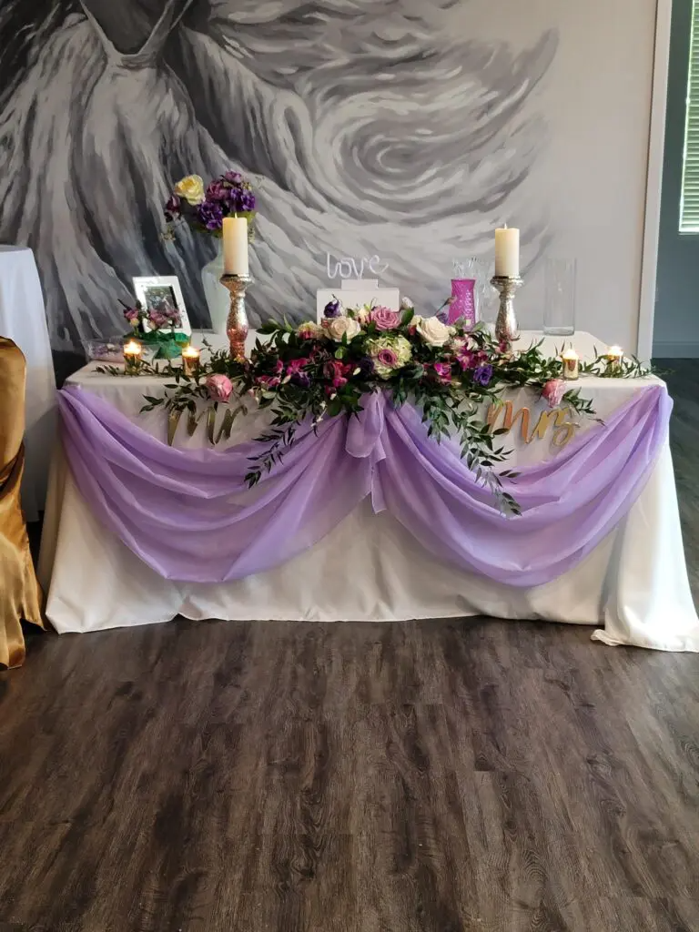 A long table with purple flowers and candles on it.