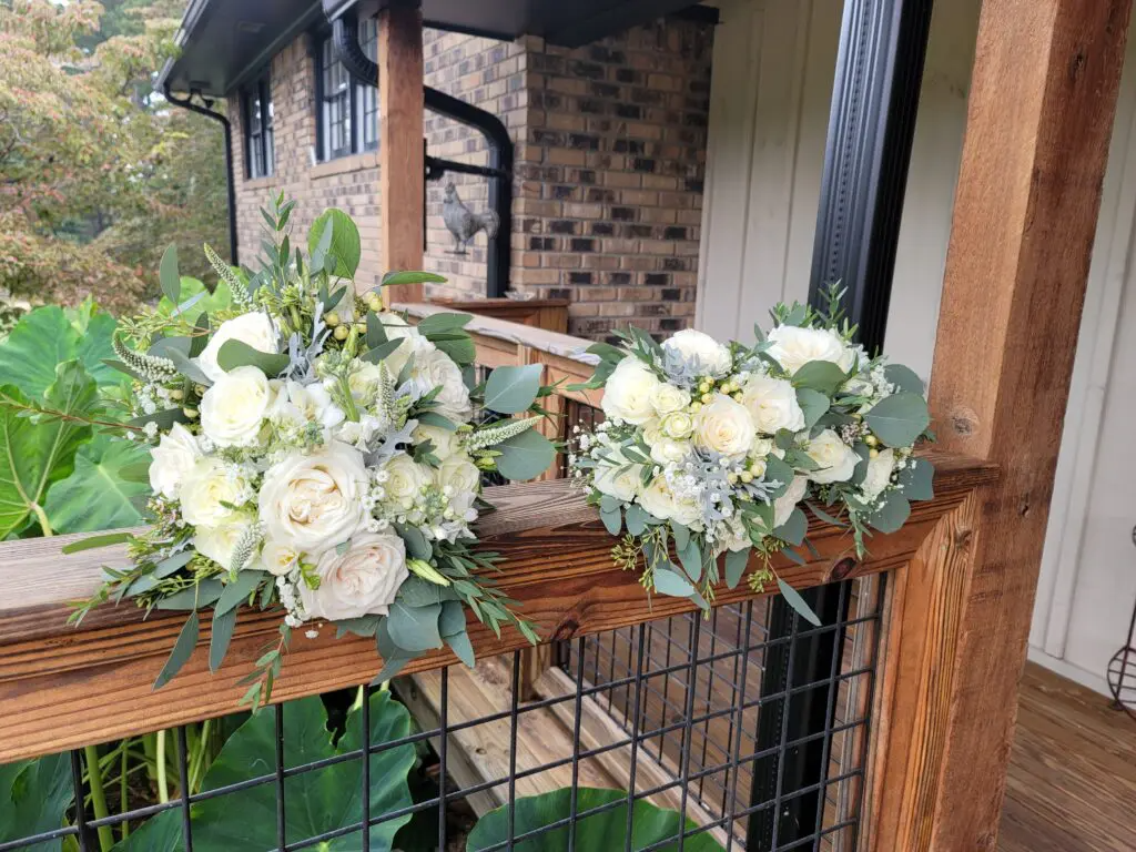 Two bouquets of white flowers are sitting on a wooden railing.